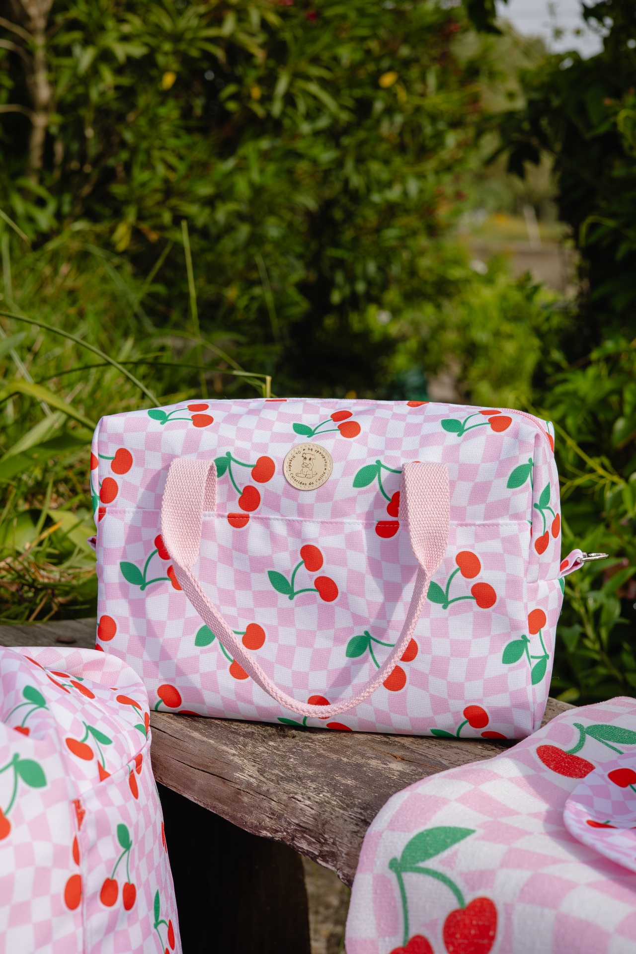Mala rosa com padrão de cerejas vermelhas e alças cor-de-rosa ao ar livre