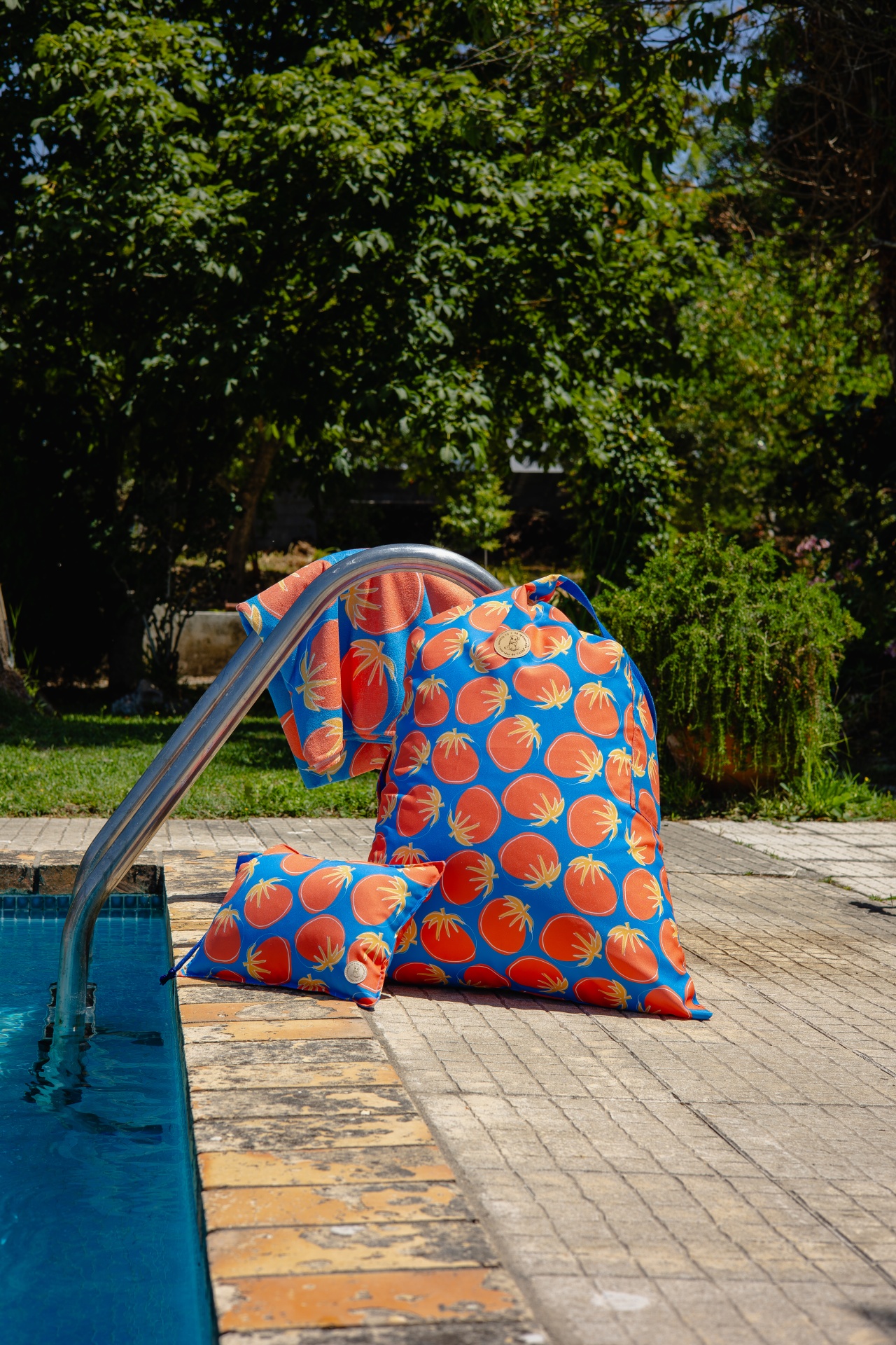 Conjunto de mochila, almofada e toalha com padrão de tomates em fundo azul junto a piscina