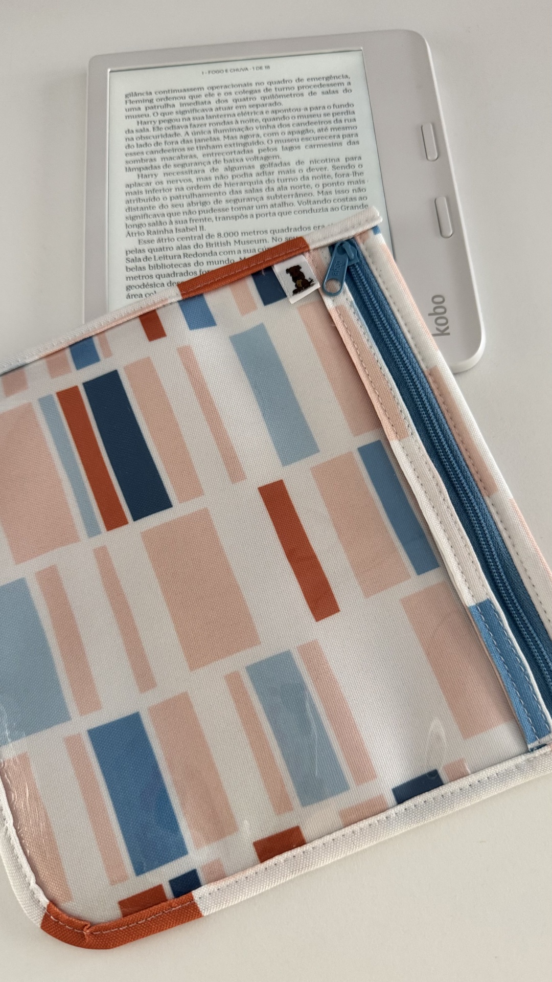 Capa protetora geométrica com fecho de correr azul enviada sobre um leitor Kobo branco com texto visível no ecrã.
