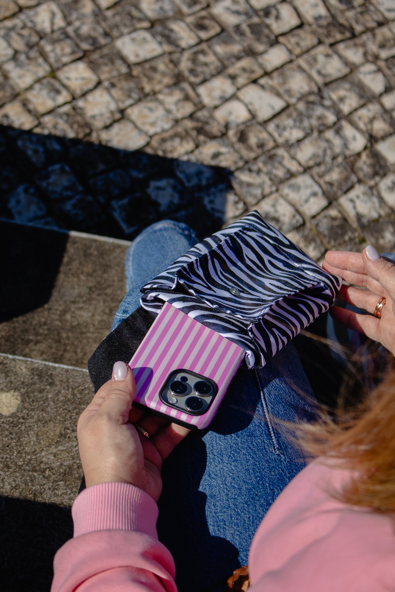 Bolsa pequena zebra com telemóvel rosa às riscas numa mão feminina sentado em escadas de pedra