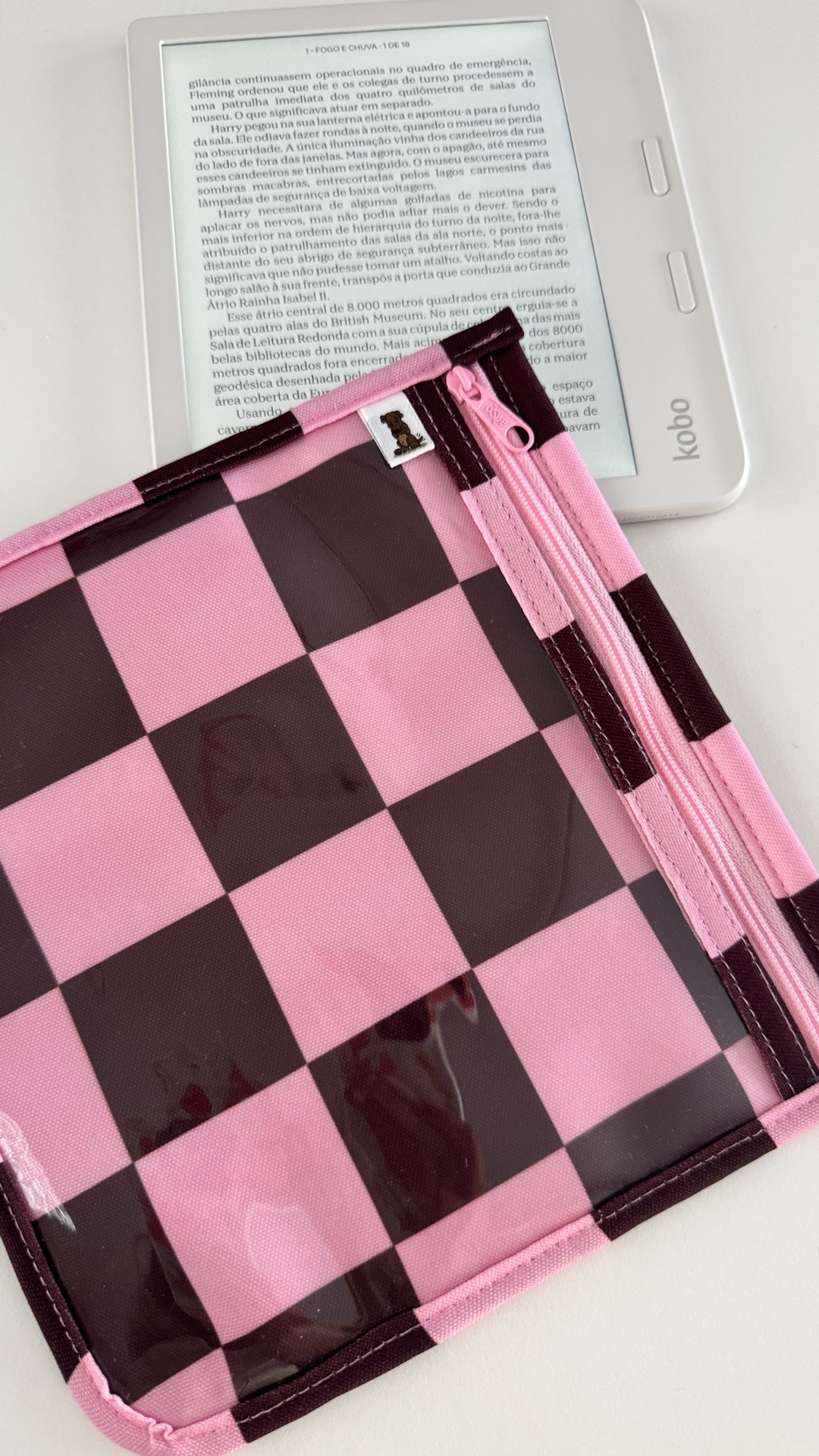 Leitor digital Kobo branco com texto em português e capa rosa castanha xadrez com fecho e símbolo de urso