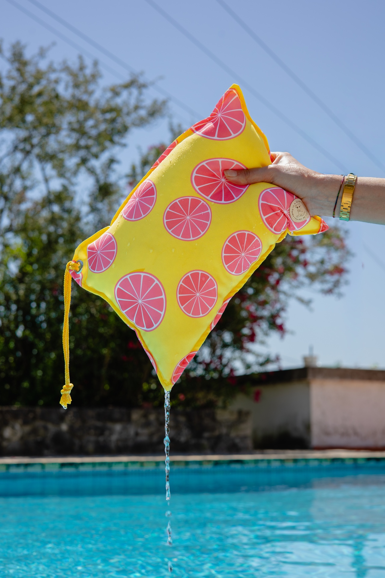 Almofada amarela com estampado de frutas e água a escorrer, vista à beira da piscina