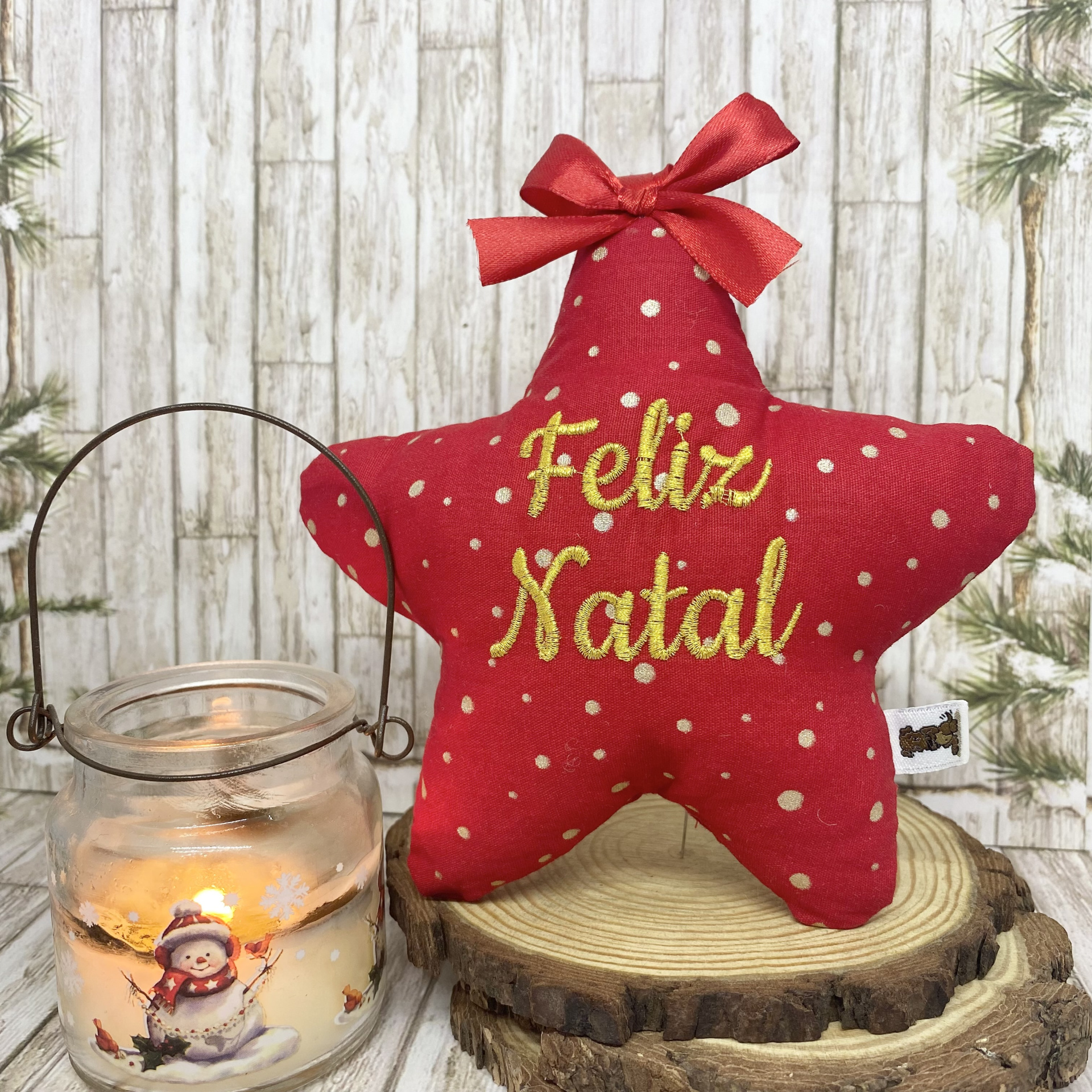 Almofada estrela vermelha com laço e texto Feliz Natal ao lado de lâmpada com boneco de neve.
