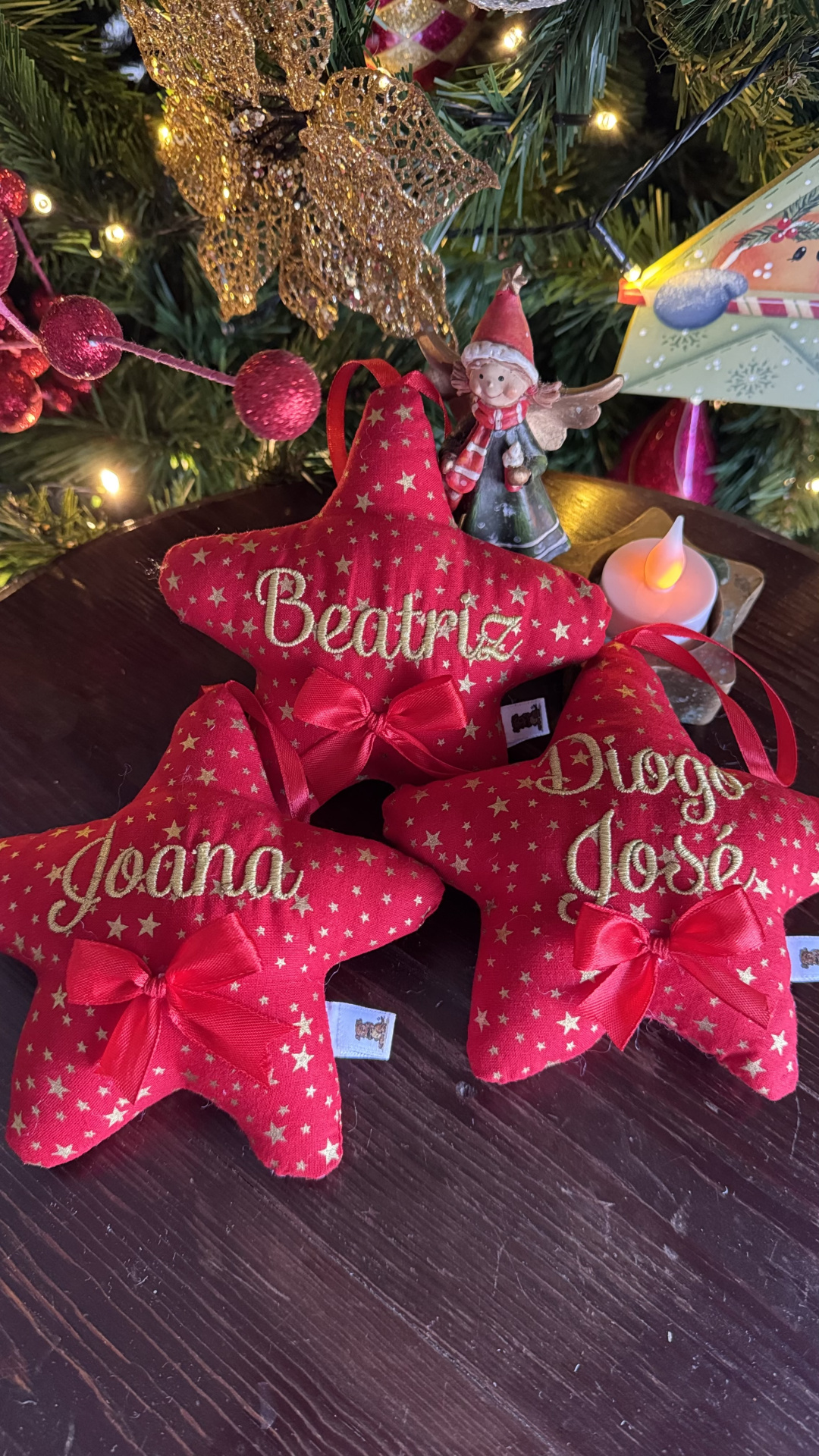 Enfeites de Natal vermelhos com nomes bordados e laços sobre mesa de madeira