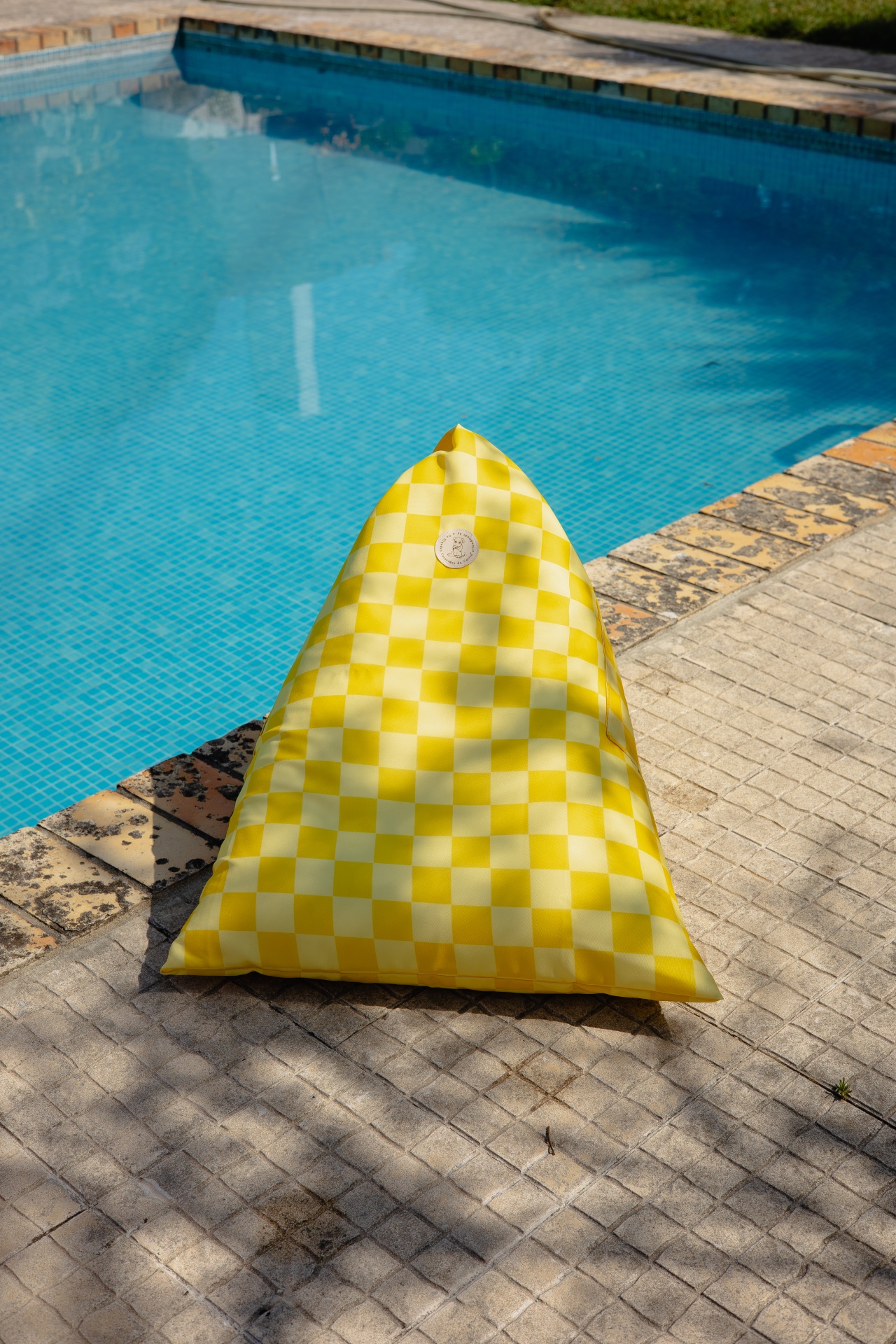 Pufe triangular amarelo e branco ao lado da piscina