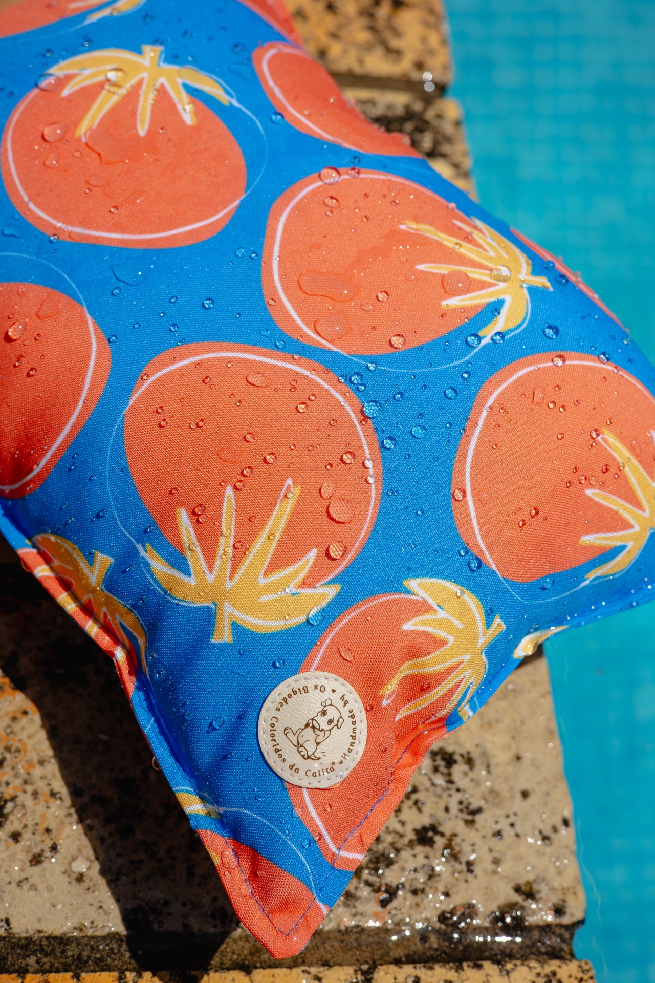 Almofada azul com padrão de tomates alaranjados perto de piscina