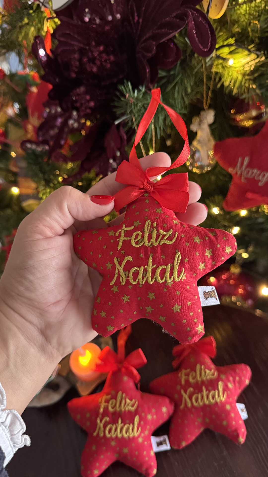 Enfeite de Natal em forma de estrela vermelha com texto Feliz Natal em dourado.