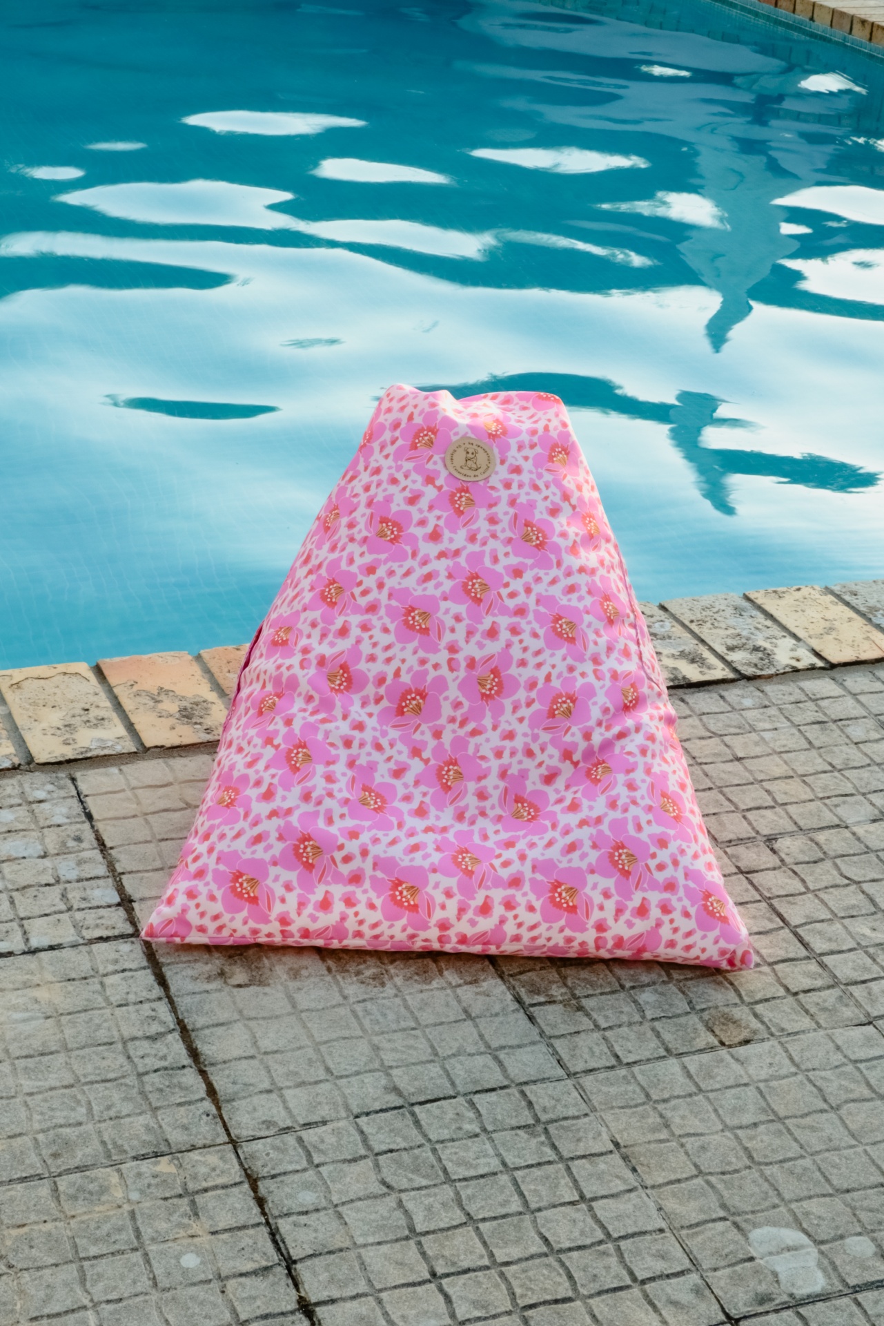 Pufe triangular floral rosa junto a piscina.