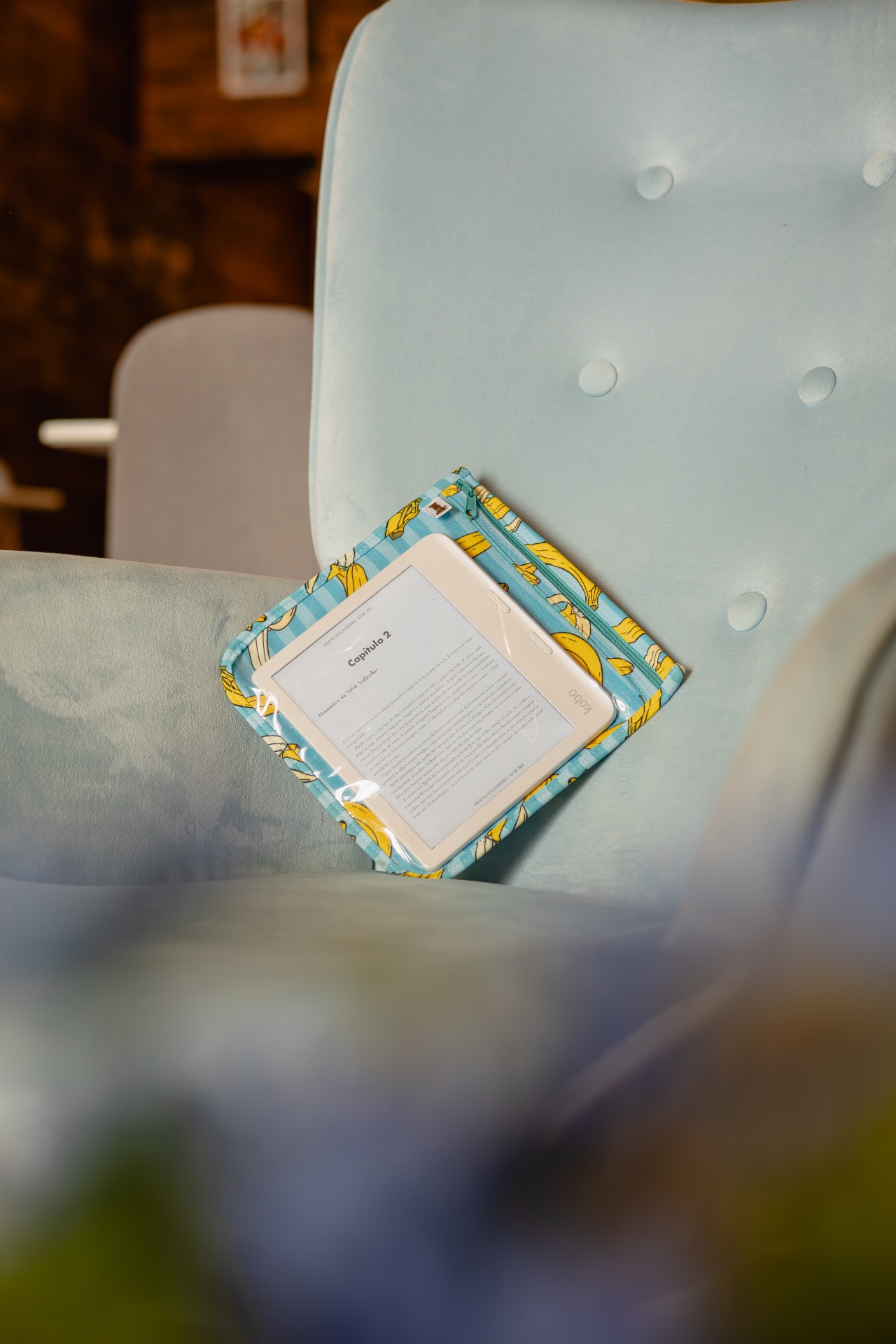 Tablet Kobo branco com capa azul de bananas amarelas numa poltrona azul clara.