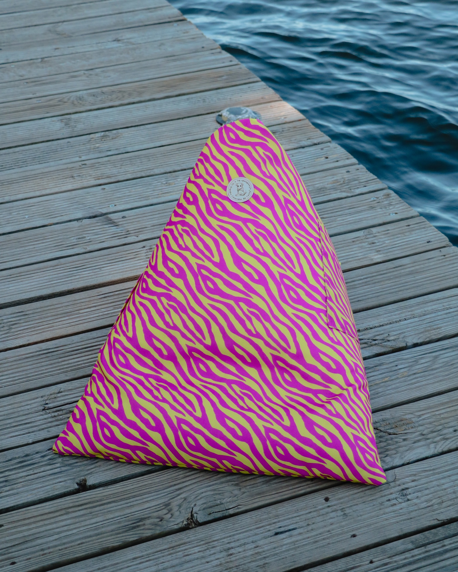 Almofada triangular rosa e amarela com padrão de riscas num cais perto da água
