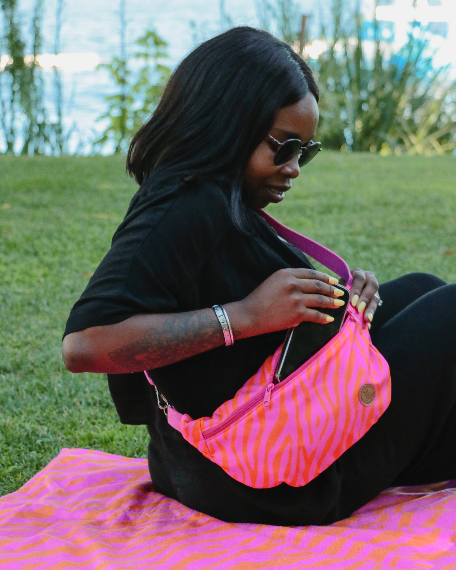 Mala de ombro rosa e laranja com padrão de ondas e mulher sentada na relva