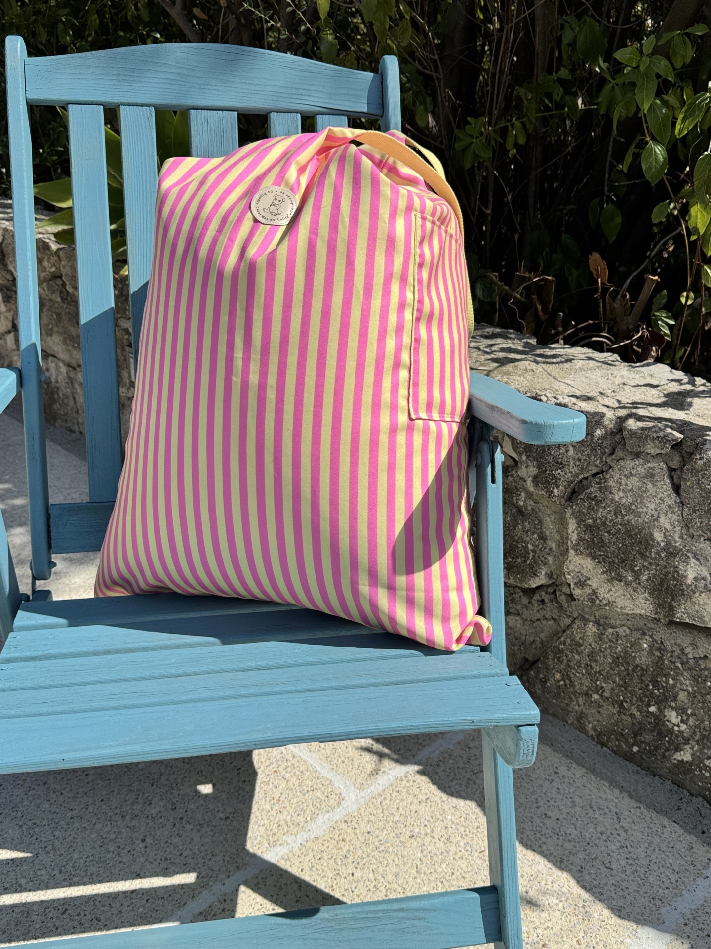 Mochila riscada rosa e amarelo numa cadeira azul ao ar livre