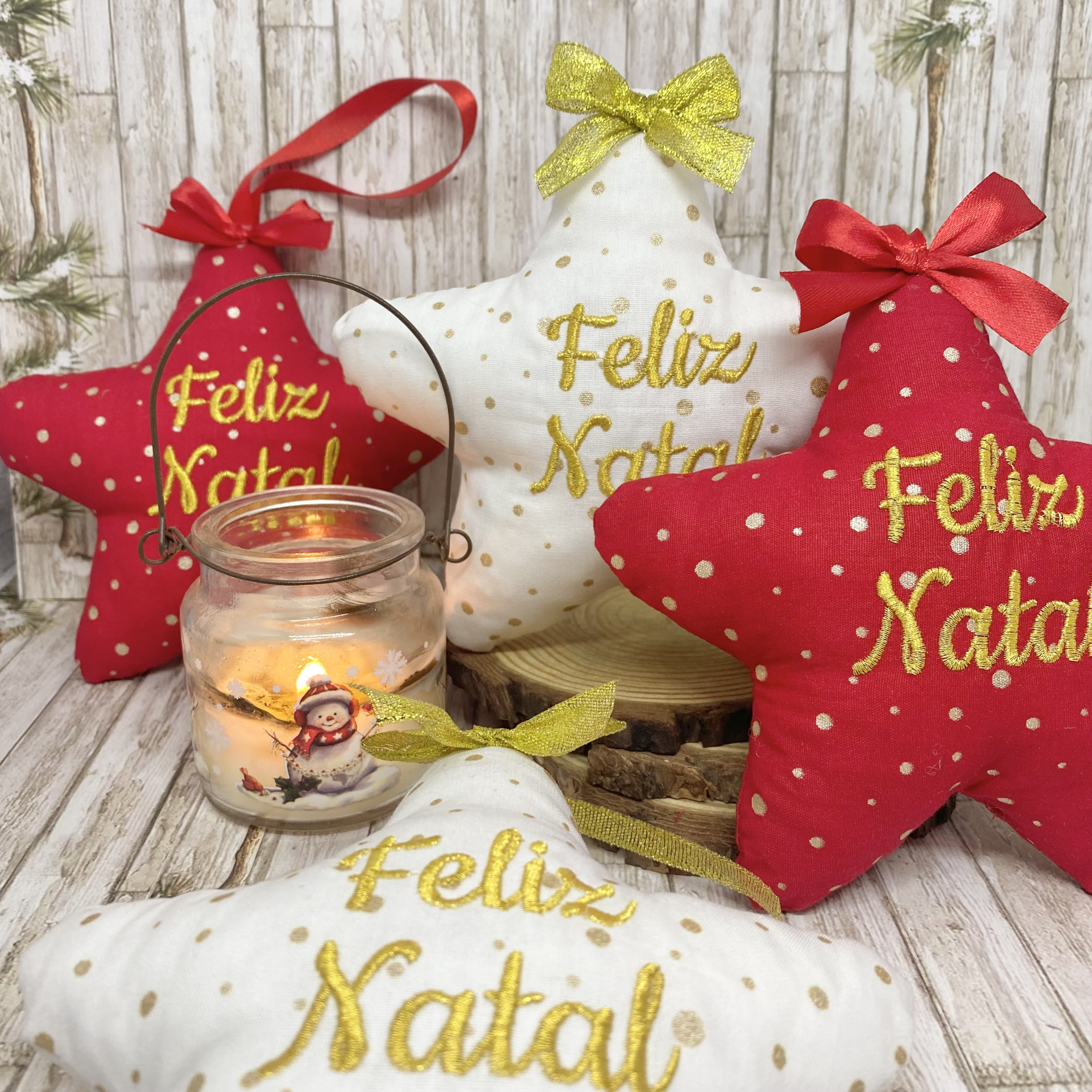 Almofadas star-shaped vermelha e branca com pontos dourados e texto Feliz Natal junto a castiçal com vela acesa