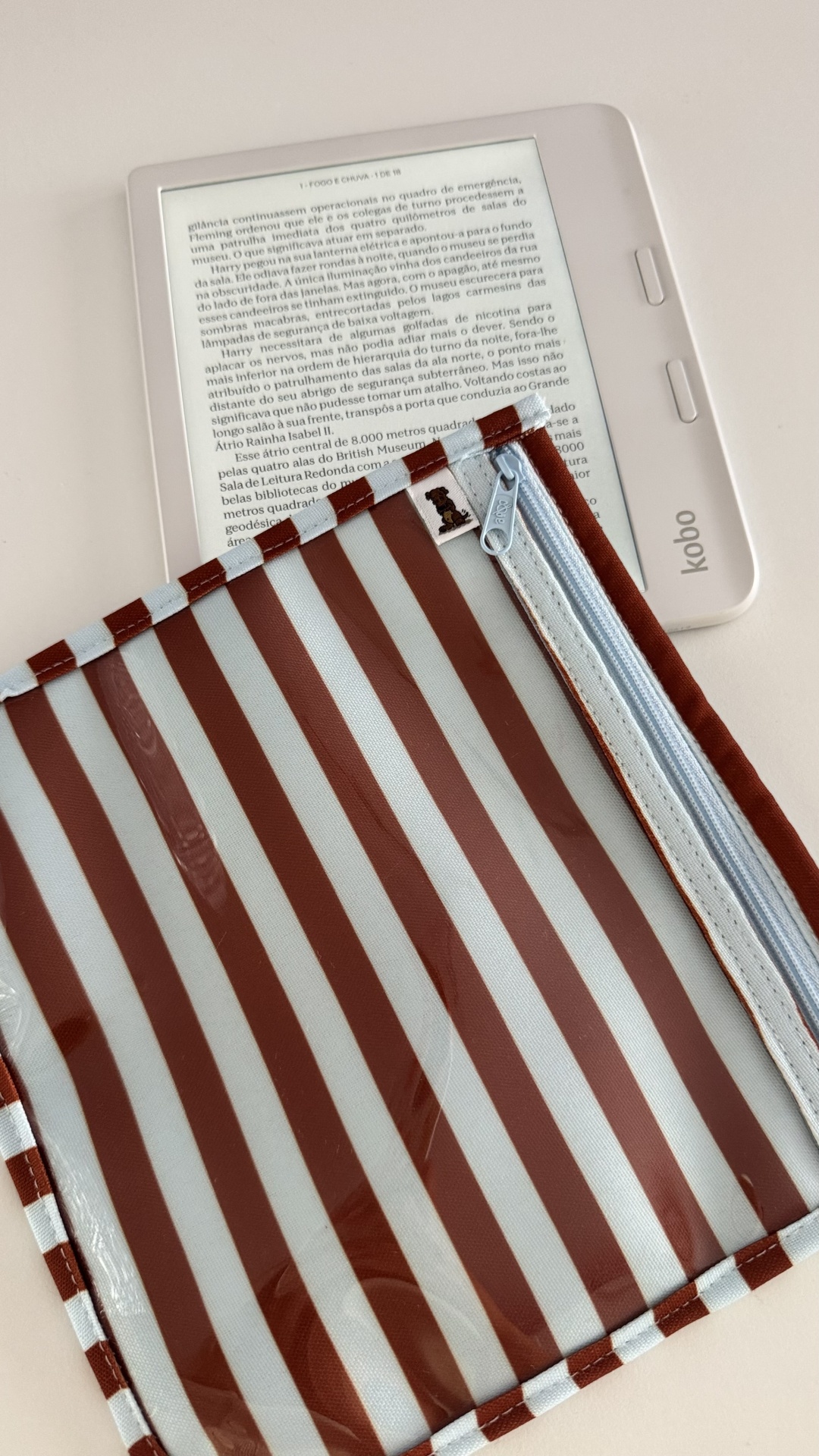 Leitor digital Kobo branco com capa transparente e bolsa riscada castanha e branca com fecho azul