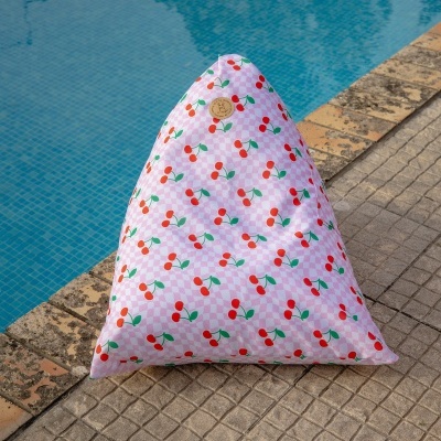 Almofada triangular rosa com padrão de cerejas ao lado de piscina azul