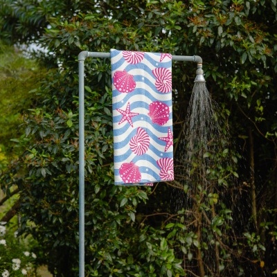Suporte de chuveiro exterior metálico com toalha decorada e natureza ao fundo