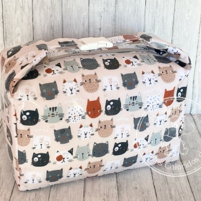Bolsa retangular com padrão de gatos coloridos em tecido sobre fundo de madeira.