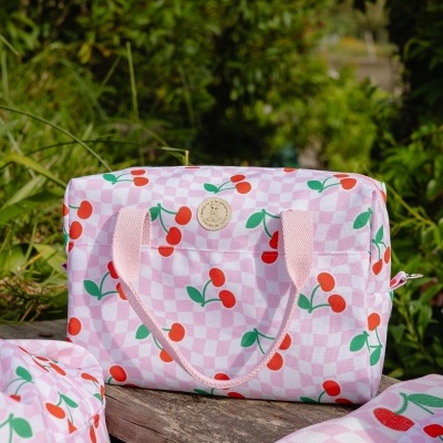 Mala rosa com padrão de cerejas vermelhas e alças cor-de-rosa ao ar livre