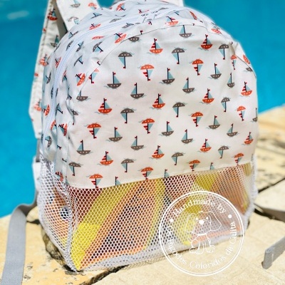 Mochila branca com padrão de barcos e guarda-sóis junto a uma piscina.