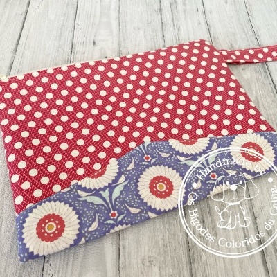 Bolsa de mão vermelha com bolinhas brancas e azul com flores sobre chão de madeira clara