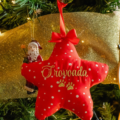 Enfeite estrela vermelho com bolinhas brancas e palavra Froivorada bordada em dourado numa árvore de Natal verde com luzes e fita dourada