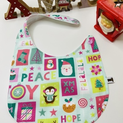 Babete de tecido com padrão natalício colorido e decoração de Natal em fundo branco