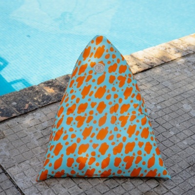 Almofada triangular azul claro com manchas laranja junto a piscina