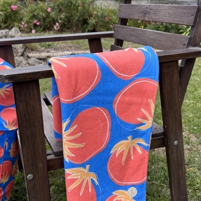 Toalha azul e vermelha com padrão de tomates numa cadeira de madeira no jardim