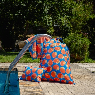 Conjunto de mochila, almofada e toalha com padrão de tomates em fundo azul junto a piscina