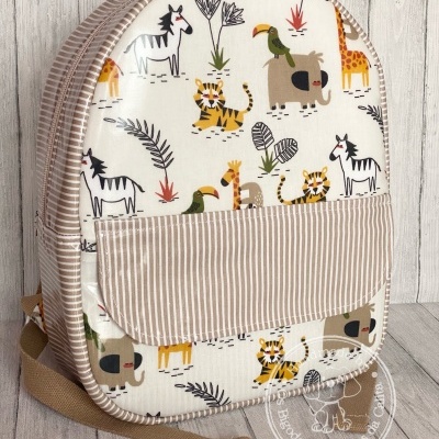 Mochila infantil estampada com animais e bolso riscado sobre fundo madeira clara