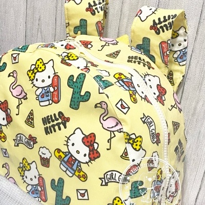 Touca infantil amarela com estampa Hello Kitty e motivos coloridos, com duas orelhas no topo