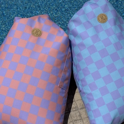 Duas almofadas com padrão quadriculado rosa e lilás e azul clara e lilás junto a piscina