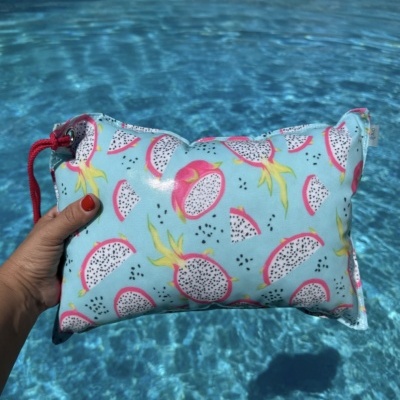 Mala azul clara com padrão de frutas do dragão segurada junto a uma piscina