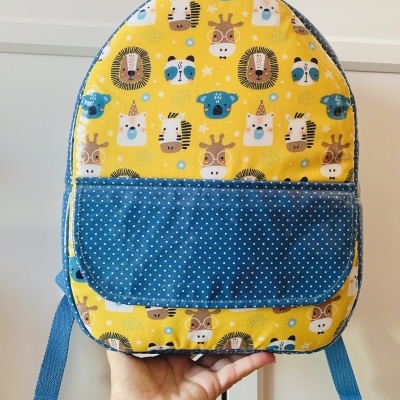 Mochila infantil em tecido amarelo com animais e bolso azul com pontos brancos.