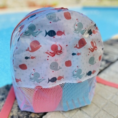 Mochila pequena com padrão de animais marinhos coloridos e bolso em rede branca perto da piscina