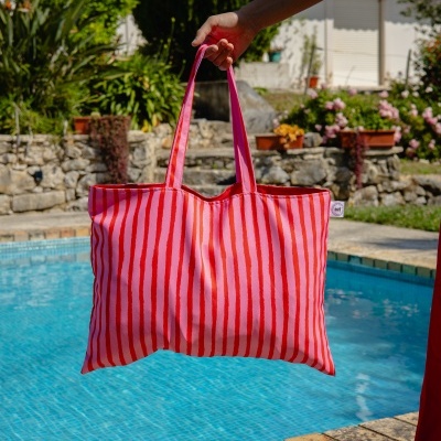 Mala de tecido rosa com riscas vermelhas junto a piscina ao sol