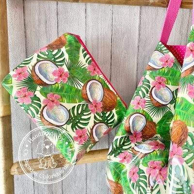 Bolsa e saco com padrão tropical de cocos, folhas e flores, pendurados num cabide de madeira clara
