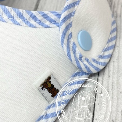 Babete branco com borda às riscas azuis e botão azul claro