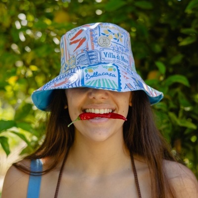 Chapéu bucket estampado colorido com palavras, pessoa com malagueta vermelha na boca e fundo de folhas verdes