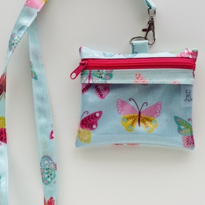 Pequeno saco azul com padrão de borboletas e fecho rosa pendurado por fita correspondente