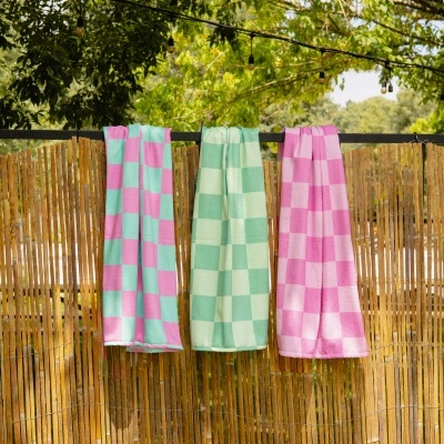 Três toalhas quadriculadas rosa e verde penduradas numa cerca de bambu com árvores ao fundo