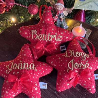 Enfeites de Natal vermelhos com nomes bordados e laços sobre mesa de madeira