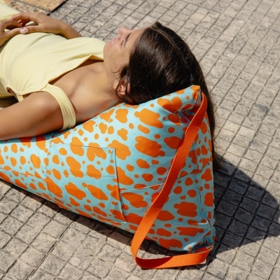 Almofada triangular azul com padrão de manchas laranjas usada ao lado de piscina