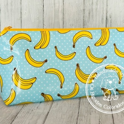 Estojo azul com padrão de bananas amarelas e fecho amarelo em superfície de madeira clara.