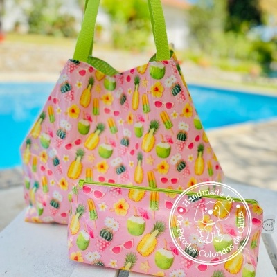 Bolsa e nécessaire rosa com padrão de frutas tropicais e alças verdes junto a piscina