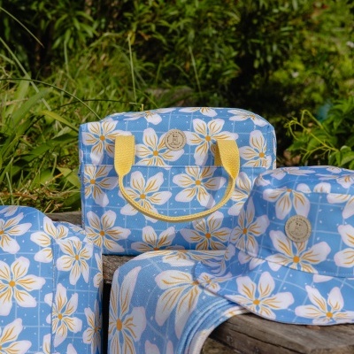 Conjunto de bolsa, chapéu e toalha com padrão floral azul e amarelo ao ar livre
