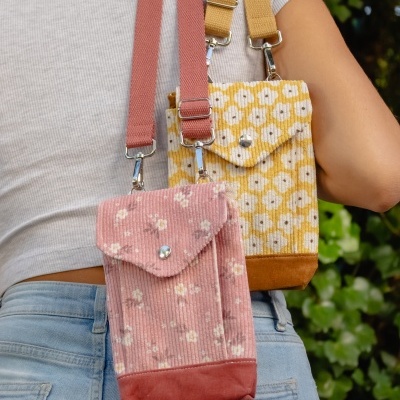 Duas bolsas pequenas de veludo cotelê com padrão floral, uma rosa e outra amarela, com alças largas, feitas em tecido ao ombro de uma pessoa.