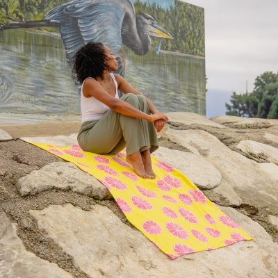 Mulher sentada sobre toalha amarela com padrão de gomos rosa ao lado de mural de ave e árvores