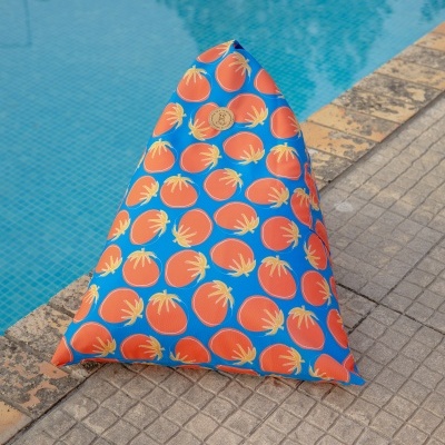 Almofada triangular azul com estampa de tomates laranja junto a piscina