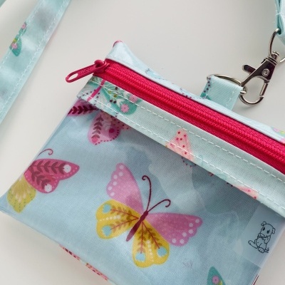 Bolsa pequena azul com padrão de borboletas e fecho rosa